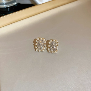 Dettaglio macro di orecchini dorati con pavé di cristalli e bordo di perle