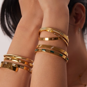 Brazaletes retro de acero dorado con circonitas esmeralda en la muñeca femenina