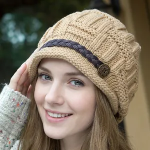 Close-up of beige knit beanie with brown leather strap and embossed vintage metal button