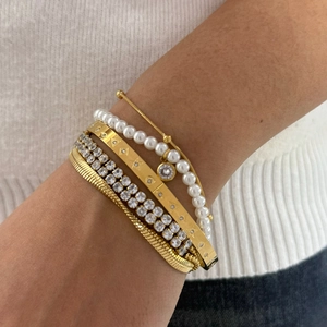 Stacked gold bracelets set with pearls and zircon crystals on a white knit background