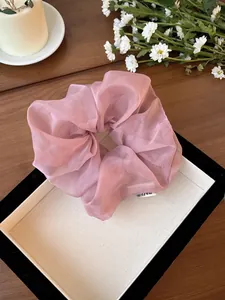 Dettaglio di elastico in organza rosa con etichetta su piatto bianco e margherite
