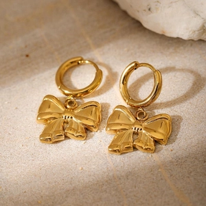 Elegant gold plated stainless steel hoop earrings with bow pendants on a stone surface