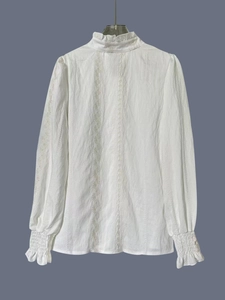 Detailed view of white long sleeve shirt with lace embroidery and pleated collar details