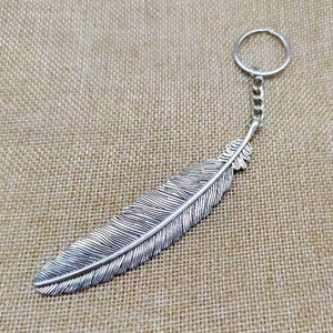 Vintage silver alloy feather keychain on rustic burlap background for car and bag decor