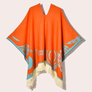 Close-up of orange ethnic poncho with blue jacquard patterns and cream fringe details