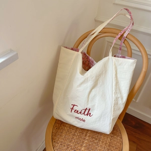 Detail of off-white tote bag with pink plaid lining and Faith mole logo text