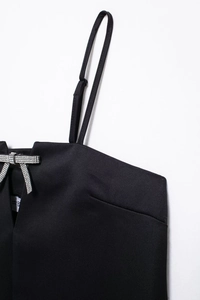 Detalle de vestido de satén negro con lazo de diamantes de imitación y tirantes
