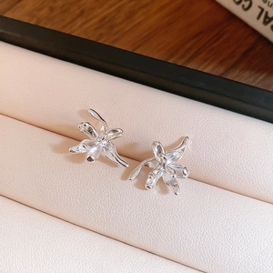 Detailed close-up of silver metal flower earrings on a soft cream leather jewelry box