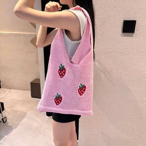Pink knitted tote bag with red strawberry embroidery worn on shoulder by a model