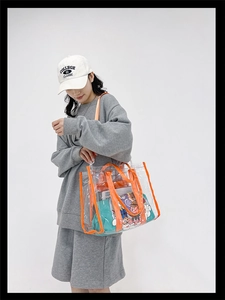 Clear PVC shoulder bag with bright orange trim shown on a model in a casual setting