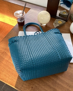 Detailansicht einer blauen geflochtenen Tragetasche auf einem Holztisch mit Lifestyle-Deko