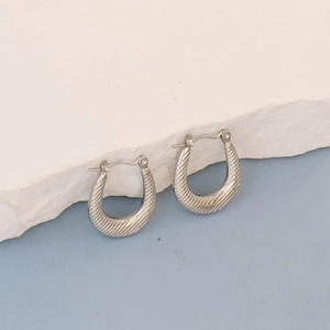 Detailed close-up of silver U-shaped oval earrings with spiral textured pattern