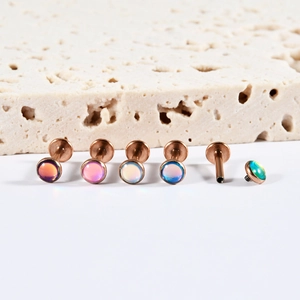 Internal threaded rose gold labret studs with colorful iridescent gems on beige stone