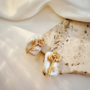 Close-up of baroque pearl earrings with golden floral patterns on natural stone