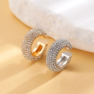 Makroaufnahme dicker Earcuffs in Gold und Silber mit weißen Strasssteinen auf Marmorstein