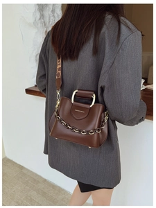 Detail of dark brown bucket bag with gold handle and printed wide fabric strap on model