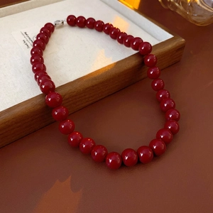 Vintage necklace with deep red round beads and silver lobster clasp in a wooden tray