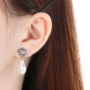Detailed close-up of Baroque pearl earring with silver textured metal on model's ear