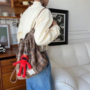 Close-up of brown plaid wool backpack with red plush charm in a cozy room setting