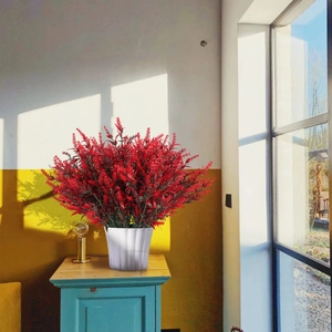 Vibrant red artificial lavender bush in white ribbed flower pot on blue side cabinet