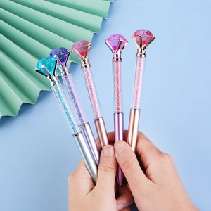 Hand holding five colorful glitter diamond pens with large crystals in various metallic tones