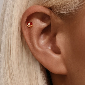 Close-up of golden s925 silver heart earring with red opal and small diamond on cartilage