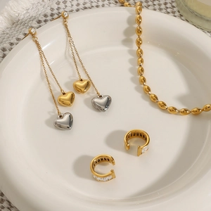 Two-tone heart tassel earrings and gold beaded necklace set on a ceramic tray