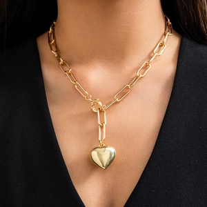 Detail view of a large gold heart pendant on a paperclip chain worn by a model