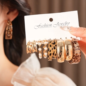 Detail of 6-pair earring set with leopard print, pearls, and gold hoops on brown fabric