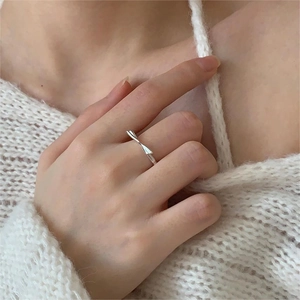 Close-up of a silver knot-shaped minimalist ring worn on finger against white knit fabric