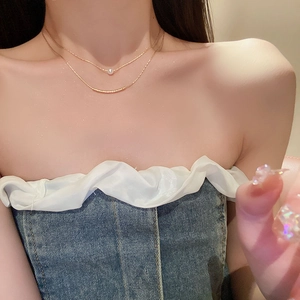 Detail of double-layer gold necklace with a white pearl and curved metal tube on a model