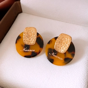 Macro shot of gold-plated earrings with tortoiseshell resin circles and Nuance script