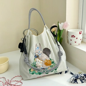 Detailed close-up of squirrel embroidery on off-white nylon shoulder bag with woven handle