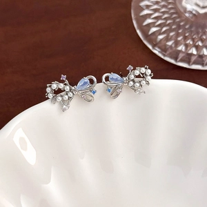 Macro shot of silver bow earrings featuring pearls and light blue gemstone accents