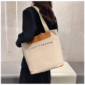Detail of beige canvas tote with brown leather handles worn by a model against marble