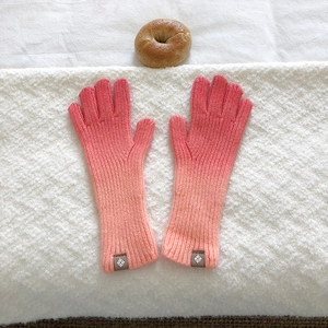 Detailed view of pink orange gradient knit gloves with ribbed texture and woven cuff label