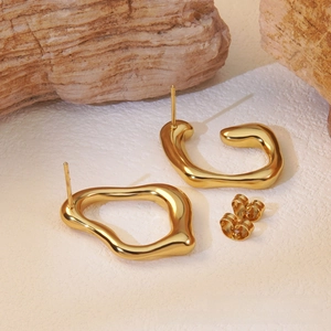 Detailed macro view of gold irregular fluid earrings on a textured stone background