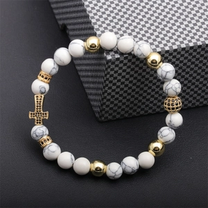 Detailed shot of white turquoise beads with a golden cross pendant and black pavé stones