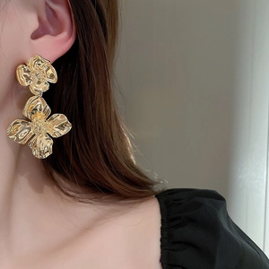 Close-up of golden double flower metallic drop earrings showing detailed relief texture