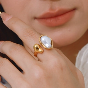 Close-up of golden stainless steel open ring featuring a baroque pearl on a model's hand