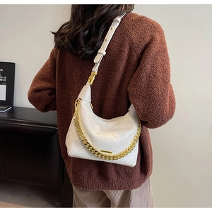 Close-up of white quilted handbag with chunky gold chain strap worn on shoulder