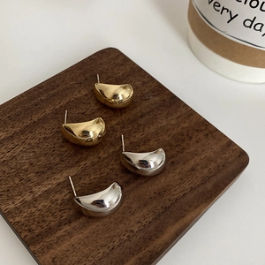 Detailed view of polished gold and silver water drop earrings on a dark wood tray