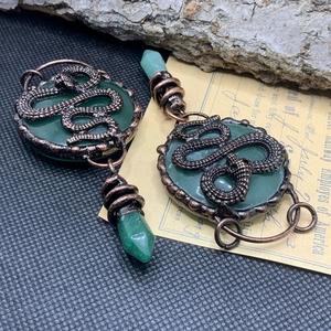 Macro detail of bronze snake wrapped around green stone pendant on vintage paper