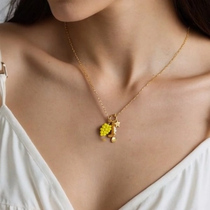Golden stainless steel necklace with grape, cowboy boot, star, and shell charms on model