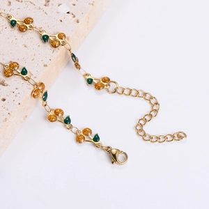 Elegant gold cherry bracelet with green leaves on textured stone, features lobster clasp