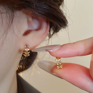 Close-up of elegant gold leaf earrings with sparkling cubic zirconia on model's ear