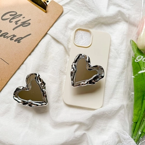 Detail of silver liquid metal heart mirror phone grip on an off-white case