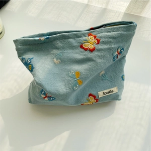 Detailed embroidery of colorful butterflies and flowers on light blue canvas pouch