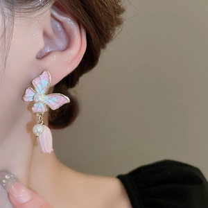 Boucles d'oreilles pendantes papillon rose et fleurs avec perles portées par un modèle