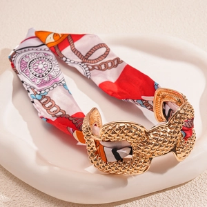 Detail of gold textured metal buckle paired with red and orange printed silk wrap bracelet
